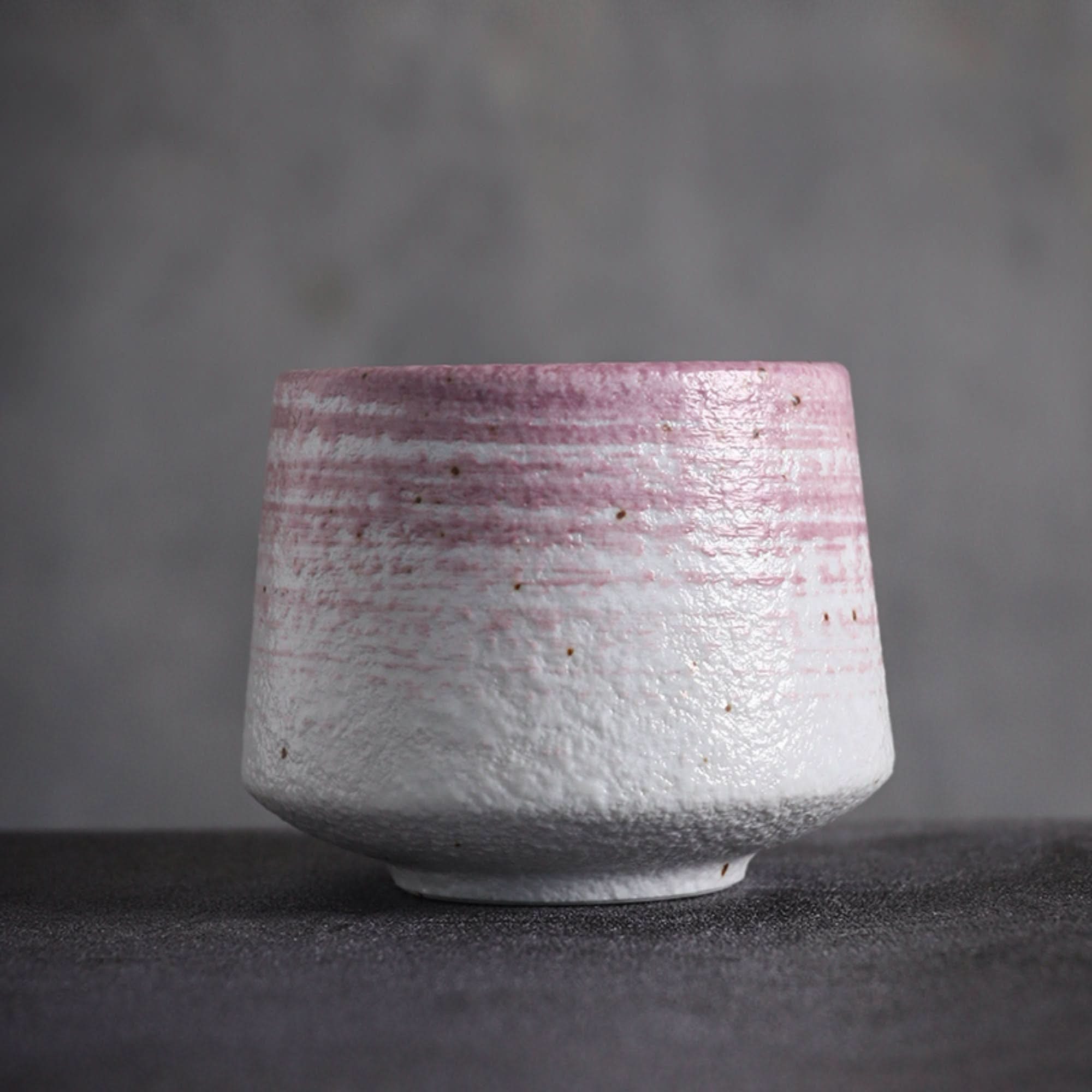 Textured Japanese tea cup with pink and gray tones on textured gray background.